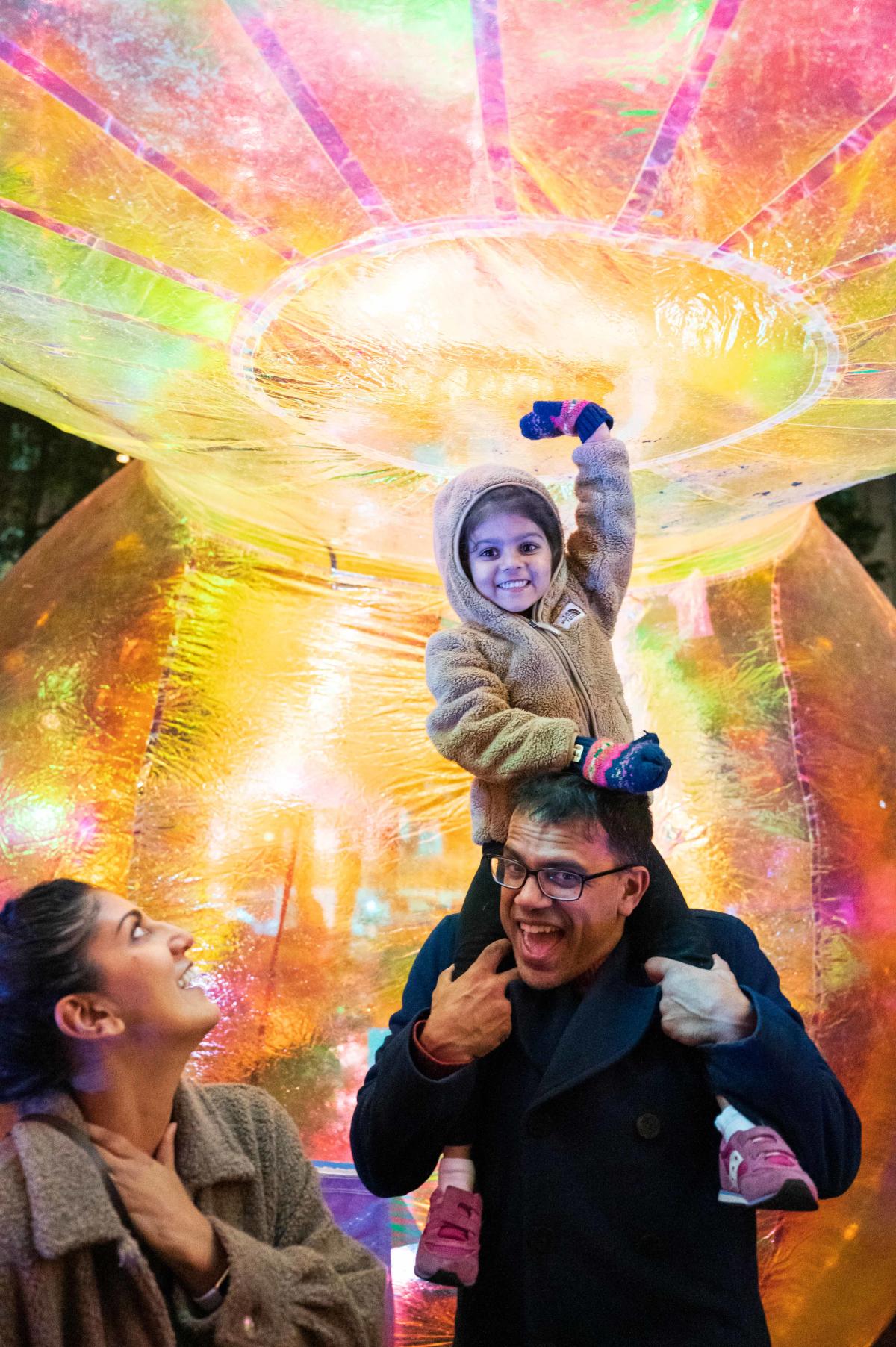 Young girl on her dad's shoulder touching a light up art display